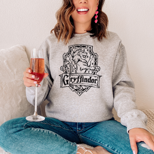 Person wearing a gray sweatshirt with Gryffindor logo, holding a glass of pink wine.